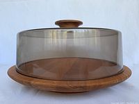 Front view of the round teak Lazy Susan server base with the clear smokey plastic lid and teak knob centered on top.