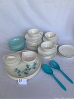 Full set from front showing cups, saucers, dinner plates with pine-needle decoration, small bowls, cream and sugar bowls, and blue plastic salad servers.
