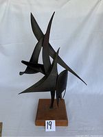 Front view of the abstract metal sculpture showing curved metal shapes mounted on teakwood base with a label '19'.