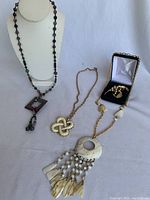 Four pieces including the natural stone necklace, mother of pearl necklace, vintage knotted pendant necklace, and floral brooch in a small box.