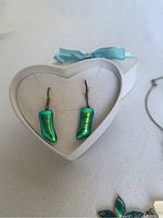 Dichroic glass earrings with iridescent green-blue teardrop shapes in sterling silver hooks, displayed in white heart-shaped box.