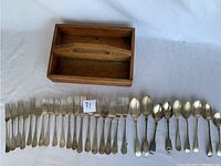 Cutlery displayed in front of the box, including multiple forks and spoons with fiddlehead style handles