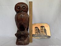 Wooden owl sculpture and enamel painting side by side with ruler for size reference