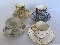 Four china tea cups with matching saucers in floral and polka dot patterns, one Shelley demitasse set with gold accents.
