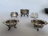 Photo showing five salt cellars, including the ornate Indian silver pair and other silver plated and cut crystal cellars