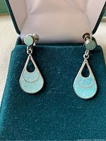 Front view of vintage sterling silver earrings with turquoise inlay, placed in a green velvet presentation box with screwback closures visible.