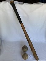 Full view of vintage Hickory baseball bat with two aged softballs positioned beside it, displaying condition and lot composition.