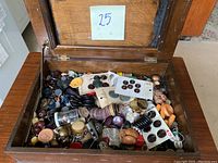 View of the open wooden hinged box filled with assorted buttons illustrating the quantity and variety.