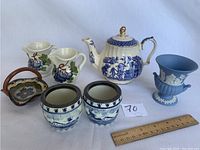 Wedgewood urn vase, Blue Willow teapot, Italian cream and sugar, Eastern European basket and pair of Delft dishes on white background with ruler for scale.