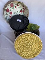 Open vintage hatbox showing interior floral lining with three vintage hats including a dark beret, a green fringed hat, and the yellow woven hat in foreground.