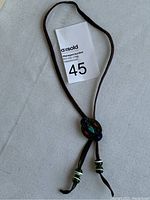 Full view of the bolo tie showing the brown leather cord and decorated centerpiece with inlaid stones and trade beads on ends.