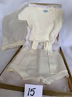Cream knitted baby romper two-piece laid in original box with tissue paper, showing top and shorts with suspender-like decorative straps.