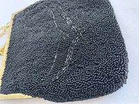 Close-up image showing texture and beadwork pattern of one black beaded purse with gold-toned frame and chain strap.