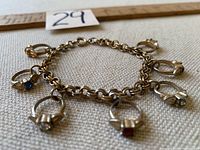 Photo of vintage gold tone charm bracelet showing seven ring-shaped charms each with different colored rhinestones, laid flat with measuring ruler and lot number visible.