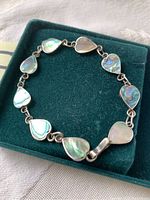 Heart link bracelet with sterling silver and abalone shell inlays displayed in a green velvet jewelry box, showing clasp and detailed inlays.