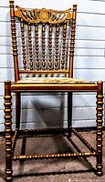 Front view of the antique wooden chair showing turned bobbin spindles on legs and back, carved decorative crest on backrest, and tapestry seat.