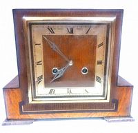Full front view of the wooden mantel clock showing the clock face, wood finish, and overall design.
