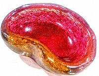 Top angled view of a red and amber thick art glass ashtray with gold flecks inside, showing the wavy and organic form.