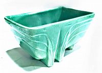 Front and side angled view of rectangular mint green glazed planter showing sculptural raised geometric and organic line details and feet support.
