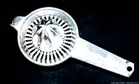 Top angled view of vintage Foley aluminum citrus juicer showing conical reamer and perforated strainer with handle.