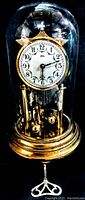 Front view of vintage glass domed mantel clock with visible clock face, pendulum, and brass base, plus winding key displayed below.
