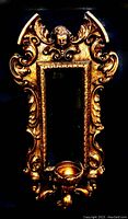 Full view of gilded ornate vintage Italian wall mirror with candle holder and cherub detail.