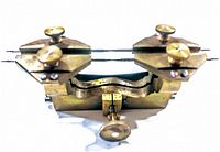 Close-up of brass vintage watch holder showing adjustable knobs and pointed prongs.