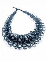 Black spiral wire necklace displayed laid flat in front view showing the interconnected rings forming the spiral design and adjustable chain clasp.