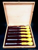 Wood carving chisels set in wooden box with velvet lining, six chisels with yellow bulbous wooden handles and metal blades.