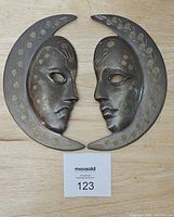 Front view of two brass crescent moon wall sculptures with detailed etched faces, shown side-by-side