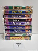 Stacked side view of 9 Disney Masterpiece Collection VHS tapes showing titles on spines including Bambi, Peter Pan, Lady and the Tramp, Mulan, The Aristocats, The Lion King, Cinderella, Snow White and Pocahontas.