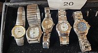 Overview of five ladies silver tone watches in a box showing front watch faces and bands, varying styles and sizes.
