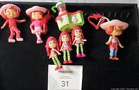 Full view of seven Strawberry Shortcake figures and one toy smoothie mixer inside black tray.