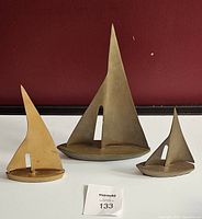 Three solid brass sailboat sculptures in decreasing sizes displayed against a red background.