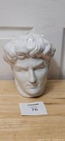 Front view of the white ceramic bust showing the detailed facial features and curly hair of Michelangelo's David sculpture, placed on a wooden surface with a lot number card.
