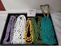 Photo showing six multi-strand necklaces in various colors laid out on a black tray.