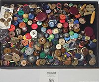 Top-down photo showing a tray filled with an assortment of vintage buttons in varying colors, sizes, and materials, including some earrings and wooden toggles.
