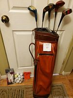 Photo of vintage golf clubs positioned inside an orange golf bag, showing the bag and club heads.