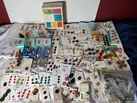 Wide view of general lot showing buttons, threads, needle threaders, and Singer machine attachments arranged on a table