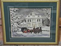 Full view of framed and matted winter scene print showing horse-drawn sleigh in front of a snow-covered Victorian mansion under snow-laden trees. Shows overall wear on frame edges.