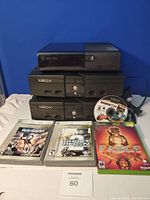 Two original Xbox consoles and one Xbox 360 console with four game cases including Fable, Madden NFL 06, Dead Rising, and Ghost Recon games displayed below the consoles.