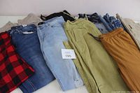 Full view of 10 pairs of men's pants in various colors and styles laid on table.