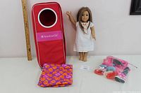 Photo of the American Girl doll standing next to the carrying case, sleeping bag laid flat, and a bag of shoes and accessories