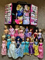 Seventeen dolls arranged in two rows with Barbie wardrobe closet open behind layering multiple clothes and accessories.