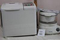 Side view of white Breadman bread maker with control panel on top and handle, next to Hamilton Beach steamer.