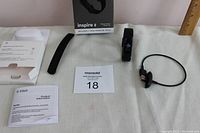 Lot contents including Fitbit Inspire 2 tracker with black wristband, extra wristband, instruction manual, charging cable, and box displayed on white surface.