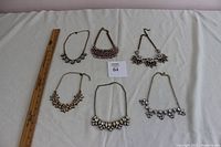 Full view of 6 necklaces arranged flat next to a 12-inch ruler for scale on a light fabric background.