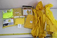 Photo showing assorted yellow rain jackets and pants, some new in packaging, others loose, arranged on a white surface with a measuring tape along the bottom.