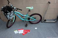 Full view of the turquoise Schwinn Deelite youth bike with purple wheels and padded floral seat, extra floral basket attached, and silver Razor scooter beside it.