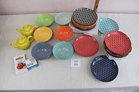 Photo showing multicolored plates and bowls arranged with two yellow ceramic teapots on left side.